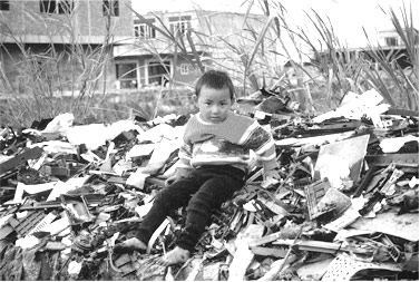  Migrant child from Hunan province sits atop one of countless piles of unrecyclable computer waste imported from around the world. Guiyu, China.